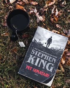 the book stephen king pet semaary is laying on the grass next to a mug