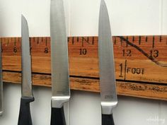 five knives are lined up on a wall with a ruler in the background and measuring tape behind them