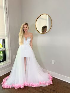 a woman standing in front of a mirror wearing a white dress with pink flowers on the skirt