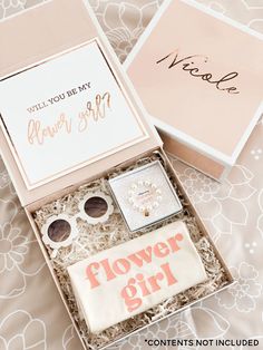 a flower girl gift box on a bed next to it's card and its contents