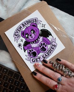 a woman's hand holding a purple bear sticker on top of a brown envelope