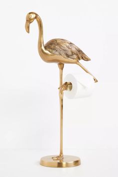 a gold flamingo standing on its hind legs in front of a white wall and toilet paper dispenser