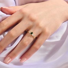 a woman's hand wearing a gold ring with a green gemstone on it