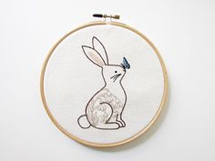 an embroidered rabbit with a blue butterfly on it's head sits in front of a white wall