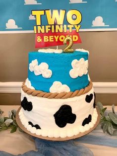 a two tiered cake decorated with blue and white frosting, topped with a cow theme