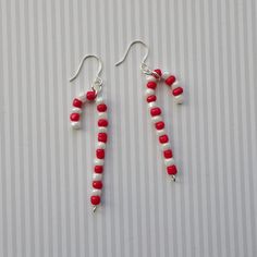 two red and white beaded earrings with silver ear wires on top of a striped background