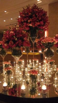 a table topped with lots of vases filled with flowers and lit candles next to each other