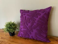 a purple pillow sitting on top of a wooden table next to a potted plant