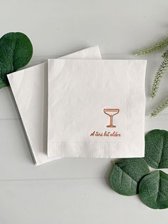 two napkins on top of each other next to some green leaves and greenery