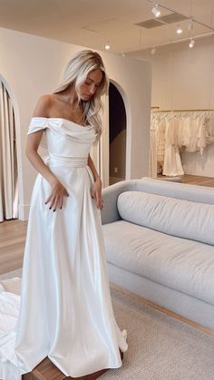 a woman in a white wedding dress looking down at her skirt while standing on the floor