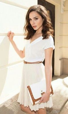 a beautiful young woman standing in front of a white wall holding a brown and white purse