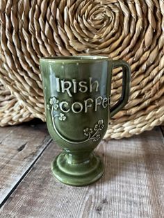 a green irish coffee mug sitting on top of a wooden table next to a wicker basket