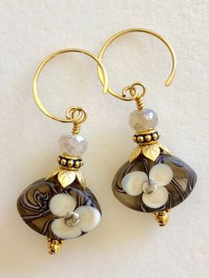 "Beautiful artisan lampwork bead earrings with hand painted white flower motif in light brown, amber, and white accented with leafy gold bead caps on 24k gold vermeil ear wires. The gorgeous translucent lampwork beads are 12 x 18 x 7mm ovals with smooth matte finish and raised floral design. Slivers of glass and fine silver are used to \"draw\" the intricate designs then beads are kiln fired at +900 degrees. The result is a unique one of a kind lampwork bead. Lovely flower beads are topped with Lamp Work Bead Jewelry, Flower-shaped Beaded Czech Glass Earrings, Glass Flower Earrings, Flower-shaped Jewelry With Colorful Czech Glass Beads, Lampwork Bead Jewelry Necklaces, Lily Earrings, Lampwork Bead Earrings, Lampwork Jewelry, Aquamarine Earrings