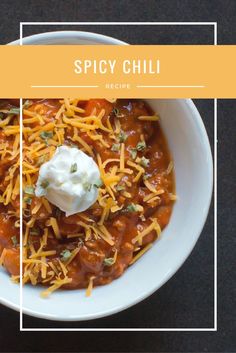 a white bowl filled with chili and cheese on top of a black table next to a spoon