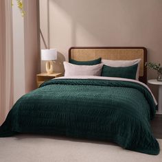 a bed with green bedspread and pillows in a neutral room next to a window