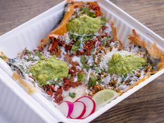 an enchilada dish in a white container with toppings on the side