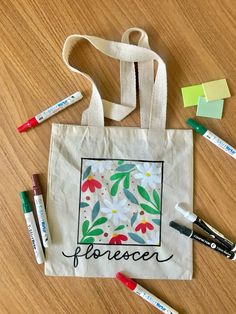 a tote bag sitting on top of a wooden table next to markers and pens