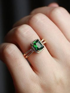 a woman's hand holding an emerald and diamond ring