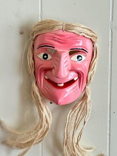 a pink mask with long blonde hair hanging on a wall