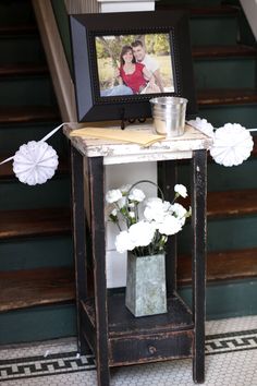 a small table with flowers on it in front of some stairs and a framed photo