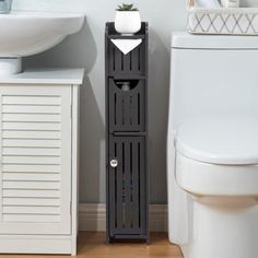 a white toilet sitting next to a sink and a tall wooden cabinet in a bathroom