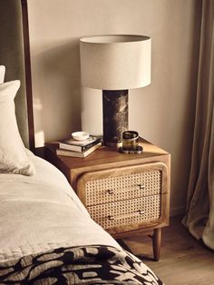 a nightstand with a lamp on top of it next to a bed and curtains in a bedroom