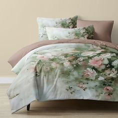 the comforter is made up and has pink flowers on it, along with two pillows