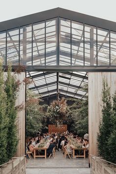 a group of people sitting around a table under a glass roofed structure with trees in the background