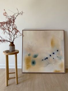 a vase with some flowers in it sitting next to a painting on the wall near a stool