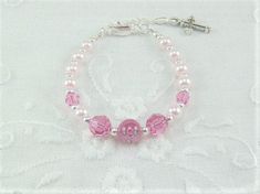 "Tiny pale pink pearls, rose Swarovski crystals and a dark pink rose lampwork bead are strung into a darling infant girl bracelet. A silver plated extension chain makes this tiny bracelet adjustable from 4 1/2\" to 5 3/4\" in length. The central bead is a dark pink Czech glass lampwork rose bead. The 4mm pale pink pearls are complimented with 4mm round rose Swarovski crystals. The 6mm Rose designed lampwork bead, along with the 6mm rose crystals are spaced with tiny silver spacer beads. A silver Pink Beaded Bracelets With 8mm Beads For Birthday, Adjustable Pink Rosary Bracelet With 8mm Beads, Personalized Pink Pearl Bracelet For Birthday, Elegant Pink Bracelets For First Communion, Personalized Pink Charm Bracelet For Wedding, Personalized Pink Rosary Bracelet For Baptism, Adjustable Pink Jewelry For Baptism, Pink 8mm Beads Jewelry For Wedding, Pink Pearl Beaded Bracelet For Birthday