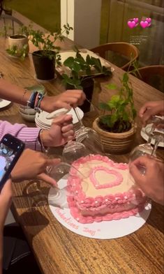 people sitting at a table with a heart shaped cake in front of them and one person holding a cell phone