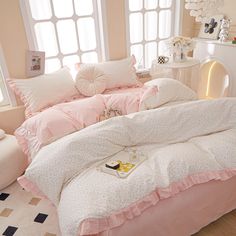 a bed with pink comforters and pillows in a room next to a window,