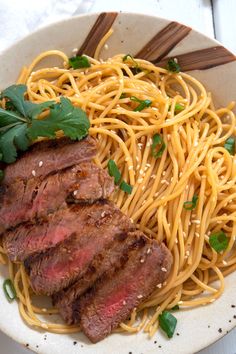 a white plate topped with meat and noodles next to chopsticks on top of a table