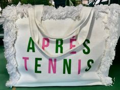 a white tote bag with the words apres tennis printed on it and fringed edges