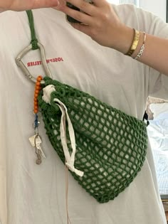 a person holding a cell phone in a green netted bag with keys attached to it