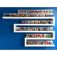 three white shelves filled with different types of action figures on top of each other in front of a blue wall