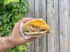 a hand holding a half eaten sandwich with meat and cheese on it in front of a wooden fence