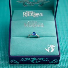 an engagement ring sits in a blue box on a turquoise tablecloth with the words,