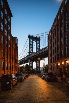 cars are parked on the street in front of tall buildings and a bridge at night