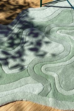 an area rug on a wooden floor with a chair and tree shadow in the background