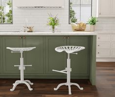 two white stools sitting in front of a kitchen island with green cabinets and counter tops