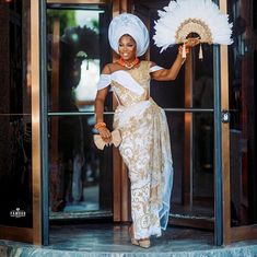 a woman in a white and gold dress is standing outside an elevator holding a fan