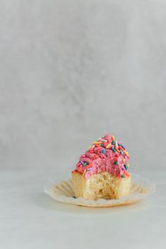 a cupcake with pink frosting and sprinkles on a paper plate