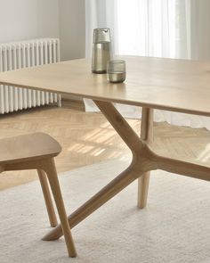 a wooden table and two chairs in front of a radiator with white curtains