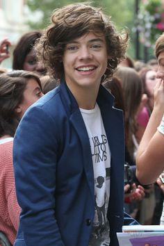 a young man standing in front of a crowd with his hands in his pockets and smiling at the camera