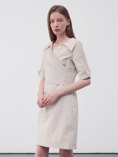 This product is a draped wrap shirt dress that elegantly combines tailored elements with a soft, feminine drape. The dress features a pronounced collar and a V-neckline, leading into a wrap front that ties at the waist, creating a figure-flattering silhouette. Its cuffed short sleeves add a structured detail to the otherwise fluid design. - The wrap style allows for an adjustable fit, catering to various body shapes.- Crafted from a light fabric, the dress is comfortable and suitable for day-long wear.- Its knee-length hem makes it versatile for both office environments and casual outings.- The draped design not only adds elegance but also ensures the dress moves beautifully with the wearer. Fitted V-neck Belted Dress For Daywear, Chic V-neck Wrap Dress With Draped Sleeves, Spring Wrap Dress With Draped Sleeves And Surplice Neckline, V-neck Midi Dress With Folds For Work, Spring Wrap Dress With Surplice Neckline For Daywear, Elegant Collared Dress With Tie Waist, Spring Surplice Neckline Wrap Dress For Daywear, Chic Belted Dress With Surplice Neckline, Elegant Belted V-neck Dress With Short Sleeves