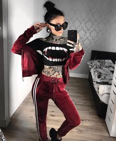 a woman with tattoos taking a selfie while wearing red tracksuits and sunglasses