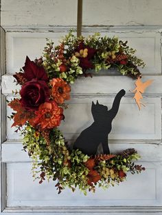 a wreath with flowers and a cat cut out of it's side hanging on a door