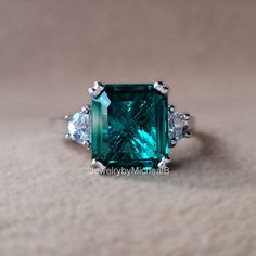 an emerald and diamond ring with three diamonds on the side, set in white gold