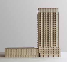 a model of a tall building made out of wooden blocks on a white table with a gray wall in the background